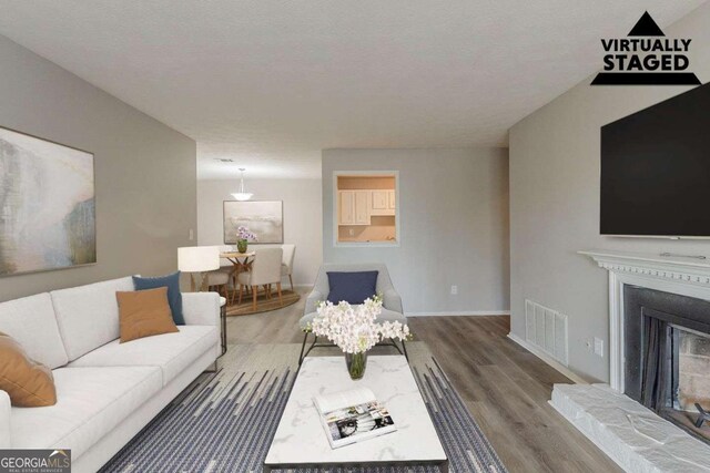 living area featuring a fireplace with raised hearth, visible vents, baseboards, and wood finished floors