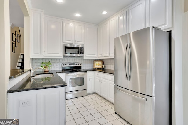 kitchen with appliances with stainless steel finishes, light tile patterned floors, a sink, and white cabinetry