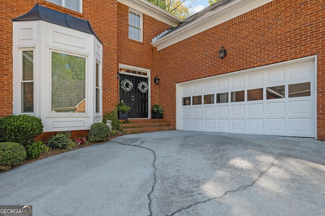 view of exterior entry featuring an attached garage, driveway, and brick siding