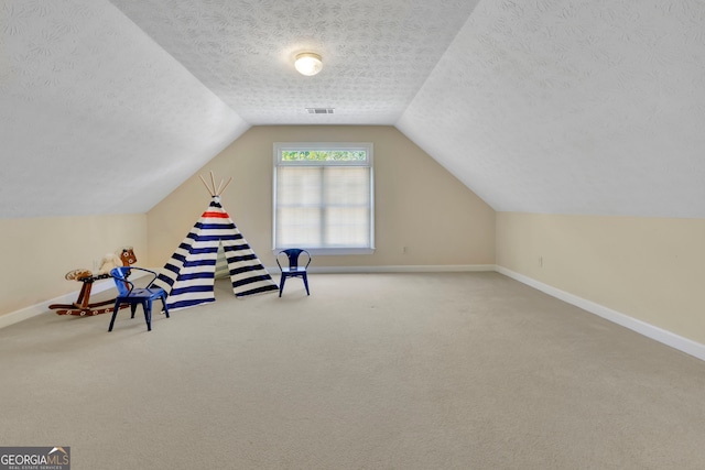 playroom featuring carpet floors, baseboards, vaulted ceiling, and a textured ceiling