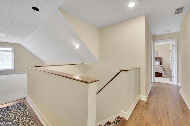 hallway featuring visible vents, light wood-type flooring, an upstairs landing, and baseboards
