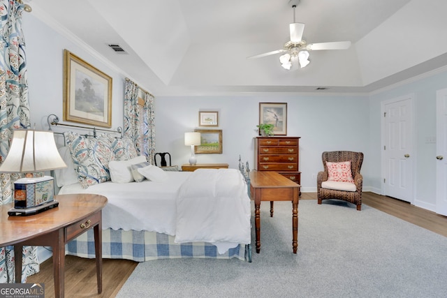 bedroom featuring a tray ceiling, ornamental molding, visible vents, vaulted ceiling, and wood finished floors