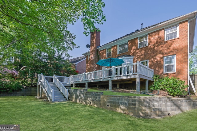 rear view of house featuring a chimney, stairs, brick siding, a yard, and a deck
