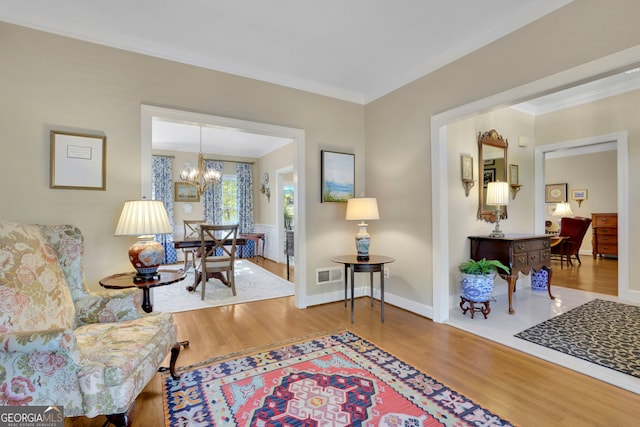 sitting room with crown molding, visible vents, a chandelier, and wood finished floors