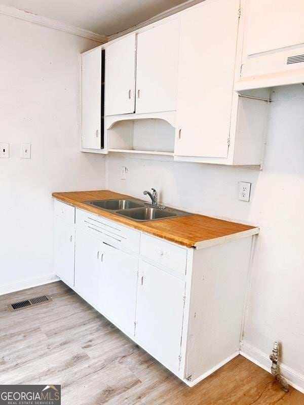 kitchen with baseboards, white cabinetry, light wood-style floors, visible vents, and a sink