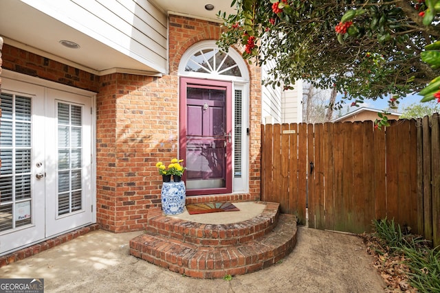 entrance to property featuring french doors, fence, and brick siding