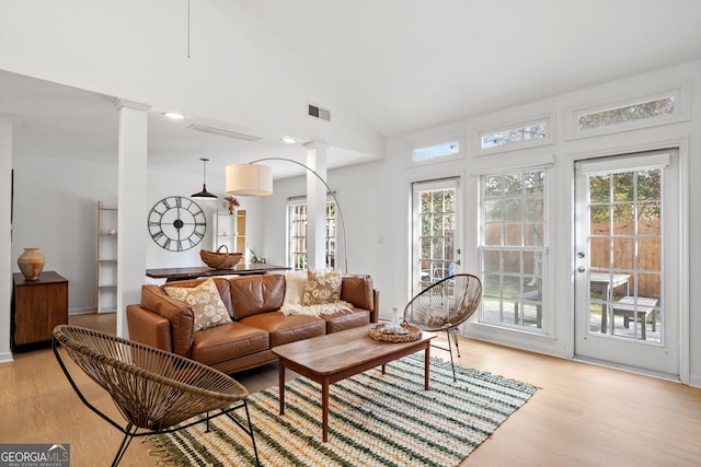 living area featuring high vaulted ceiling, light wood finished floors, visible vents, and ornate columns
