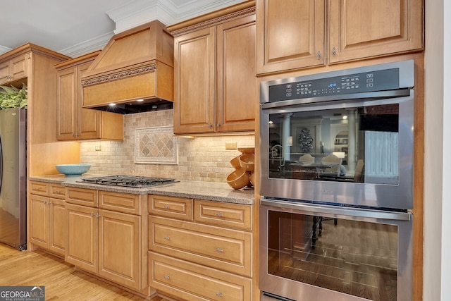 kitchen with light wood-style flooring, light stone counters, custom range hood, stainless steel appliances, and decorative backsplash