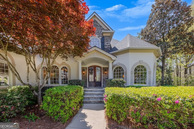 view of exterior entry featuring french doors, a shingled roof, stucco siding, and stone siding
