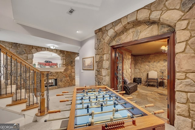 recreation room with a fireplace, ornamental molding, and visible vents