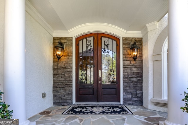 doorway to property with a porch, french doors, stone siding, and stucco siding