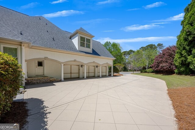 view of side of home with an attached garage, roof with shingles, driveway, and stucco siding