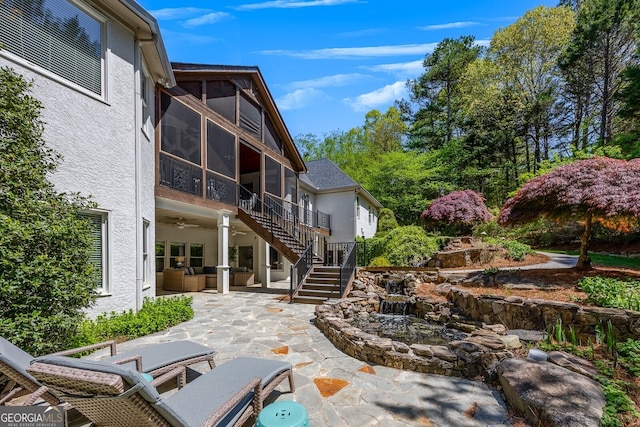 back of property featuring a sunroom, stucco siding, a ceiling fan, a patio, and stairs