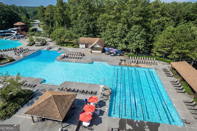 pool featuring a patio area, a water slide, and a wooded view