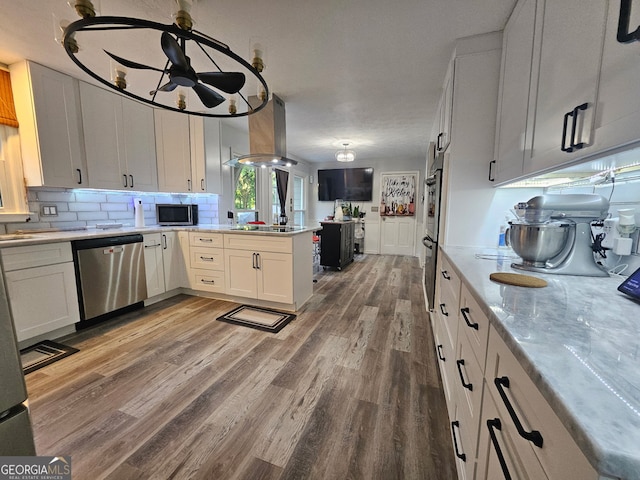 3650 Bay Leaf Dr, Loganville, GA 30052 - kitchen featuring appliances with stainless steel finishes, island range hood, light wood finished floors, a peninsula, and backsplash