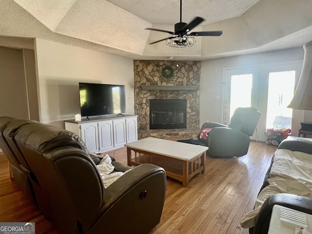 living room with a fireplace, light wood-type flooring, a textured ceiling, and ceiling fan