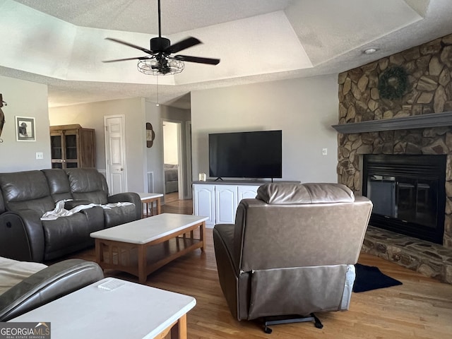 living room with a textured ceiling, wood finished floors, a fireplace, and a ceiling fan