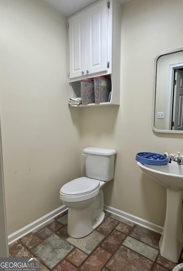 half bath featuring stone finish flooring, baseboards, and toilet