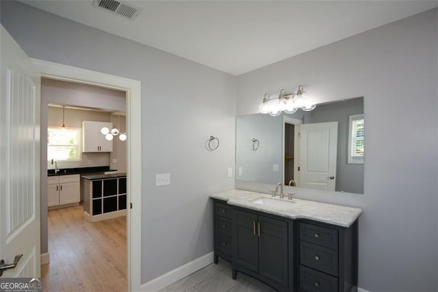 bathroom featuring baseboards, visible vents, a notable chandelier, wood finished floors, and vanity