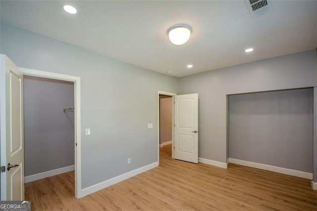 unfurnished bedroom with recessed lighting, light wood finished floors, visible vents, a walk in closet, and baseboards