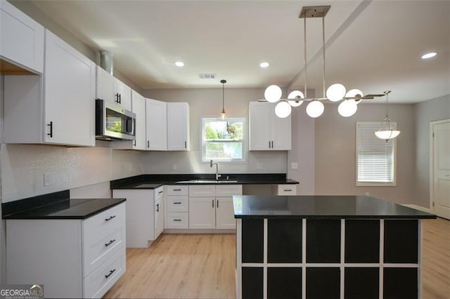 kitchen featuring stainless steel microwave, dark countertops, a sink, and light wood-type flooring
