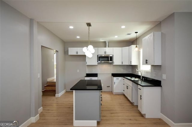 kitchen with baseboards, a kitchen island, appliances with stainless steel finishes, light wood finished floors, and a sink