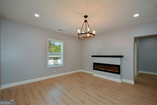 unfurnished living room featuring a glass covered fireplace, a notable chandelier, light wood-type flooring, and baseboards