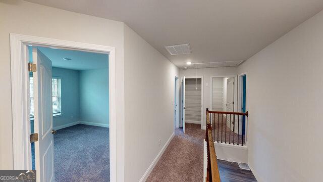hallway with an upstairs landing, visible vents, baseboards, and carpet floors