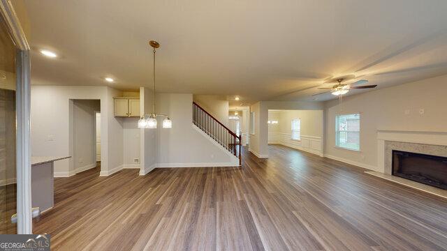unfurnished living room featuring baseboards, ceiling fan, a high end fireplace, stairway, and wood finished floors