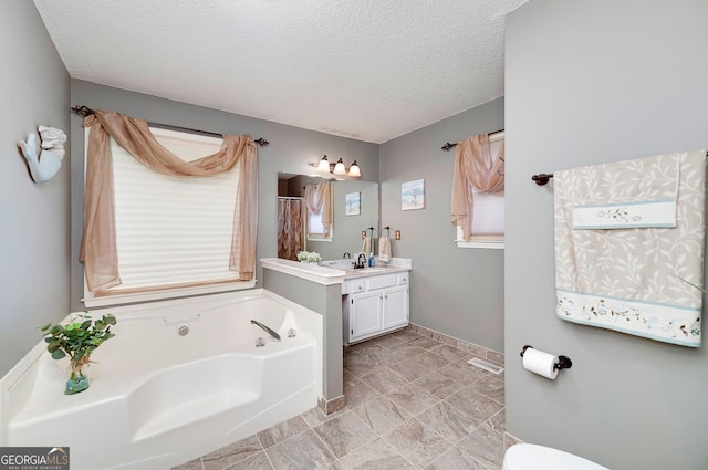 bathroom with a garden tub, a textured ceiling, a healthy amount of sunlight, and vanity