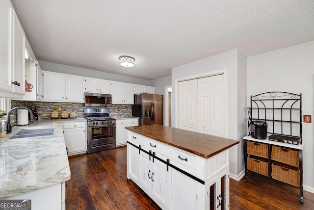 kitchen with dark wood-style flooring, appliances with stainless steel finishes, tasteful backsplash, a sink, and white cabinets