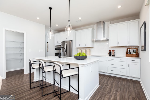 kitchen featuring stainless steel appliances, dark wood-style floors, an island with sink, and wall chimney range hood
