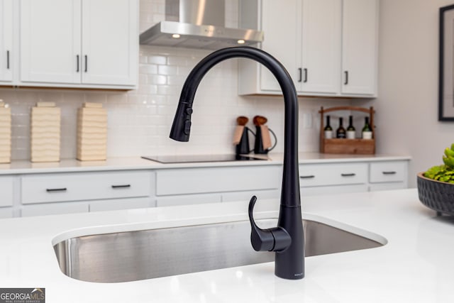 details featuring black electric cooktop, tasteful backsplash, white cabinetry, wall chimney range hood, and light countertops