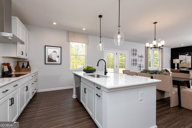kitchen with dark wood-style floors, a sink, baseboards, a notable chandelier, and wall chimney range hood