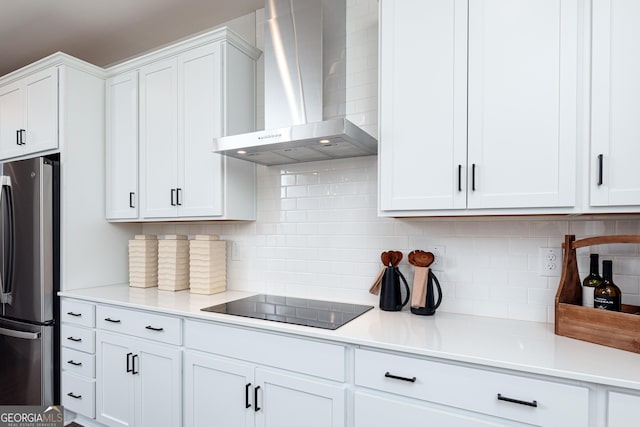 kitchen featuring freestanding refrigerator, wall chimney exhaust hood, white cabinetry, and black electric stovetop