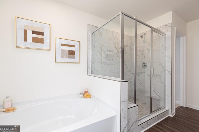 bathroom with a shower stall, baseboards, a bath, and wood finished floors