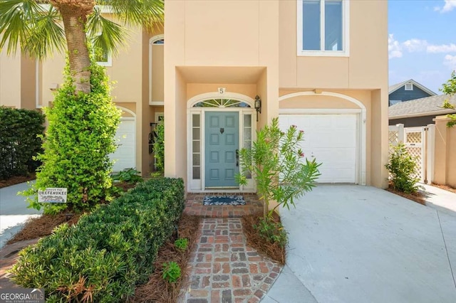 property entrance featuring fence, a garage, stucco siding, and driveway