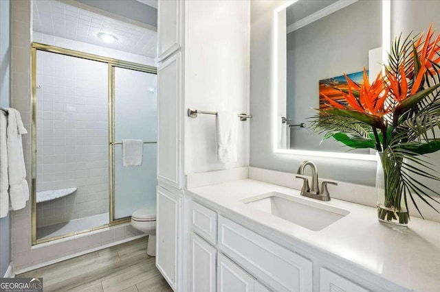bathroom featuring crown molding, vanity, toilet, wood finished floors, and a stall shower