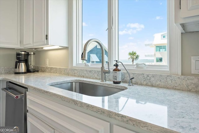 kitchen featuring stainless steel dishwasher, white cabinetry, a sink, and light stone counters