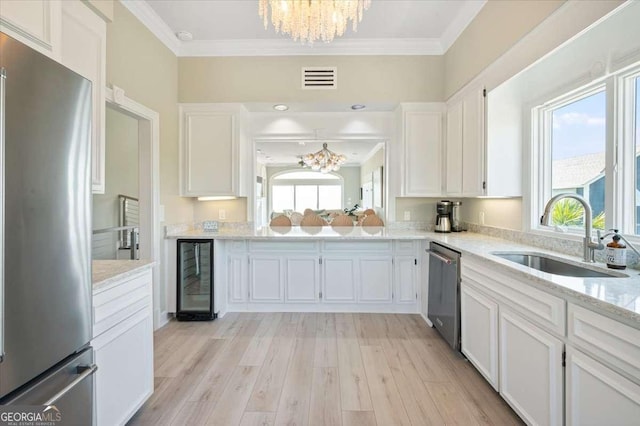 kitchen with a sink, ornamental molding, a chandelier, wine cooler, and stainless steel appliances