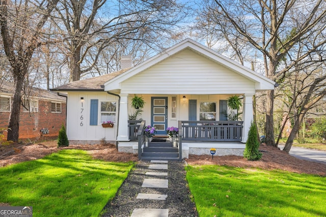 bungalow-style home with roof with shingles, a chimney, a front lawn, and covered porch