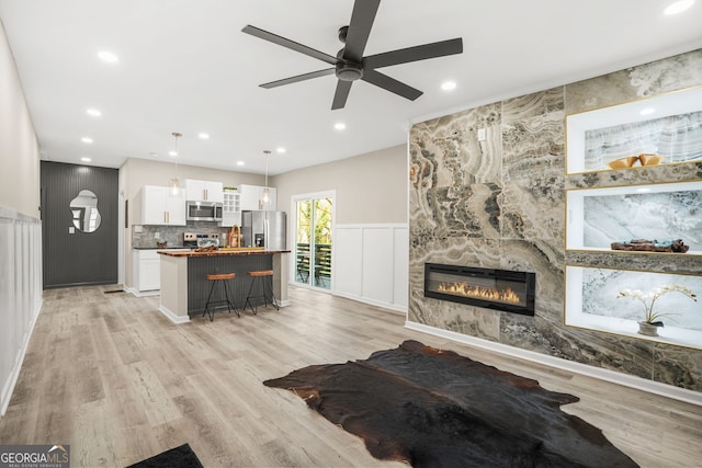 living room featuring light wood-style floors, ceiling fan, a large fireplace, and recessed lighting