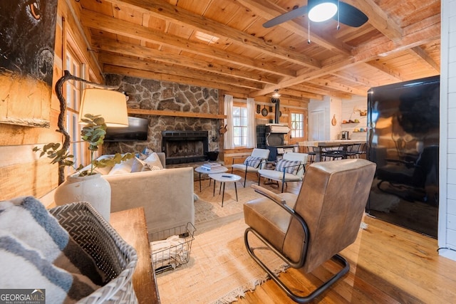 living room featuring beamed ceiling, a ceiling fan, a stone fireplace, wooden ceiling, and hardwood / wood-style flooring