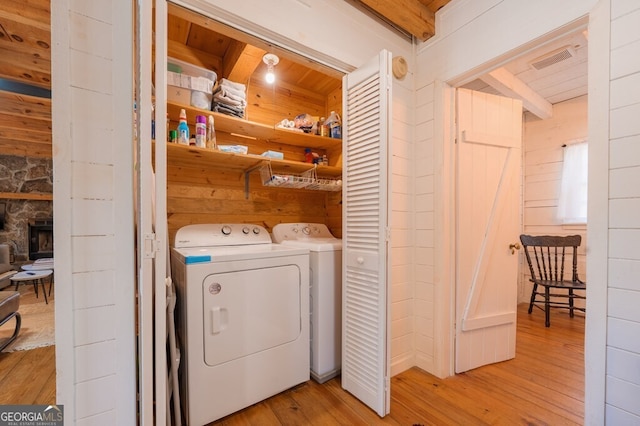 clothes washing area with a fireplace, wooden walls, light wood-style flooring, washer and clothes dryer, and laundry area