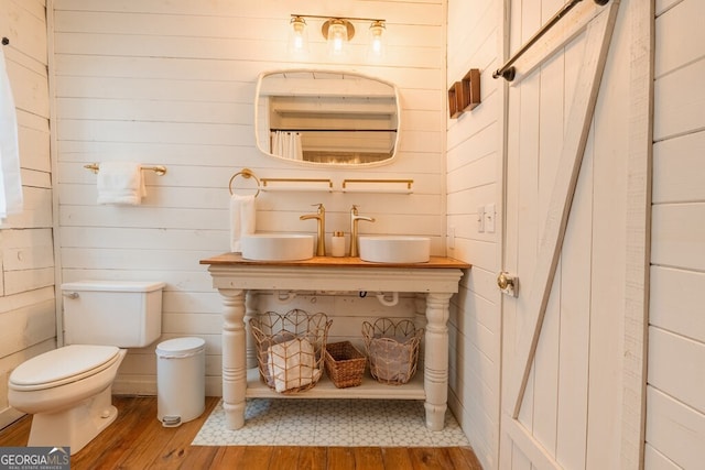 full bath with a sink, toilet, hardwood / wood-style flooring, and wooden walls