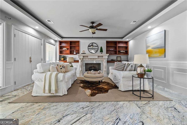 living room with a decorative wall, visible vents, marble finish floor, and ceiling fan