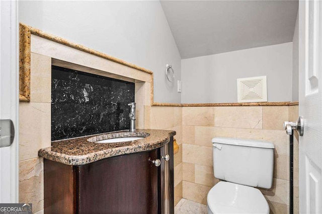 bathroom featuring lofted ceiling, a wainscoted wall, toilet, vanity, and tile walls