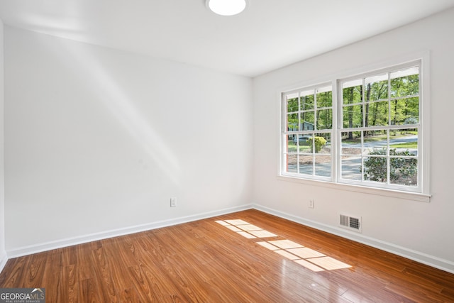 unfurnished room featuring wood finished floors, visible vents, baseboards, and a healthy amount of sunlight