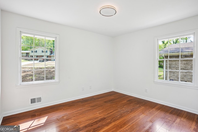 empty room with dark wood finished floors, baseboards, a healthy amount of sunlight, and visible vents