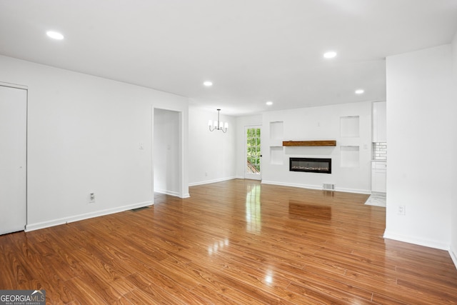 unfurnished living room featuring recessed lighting, wood finished floors, visible vents, a chandelier, and a glass covered fireplace